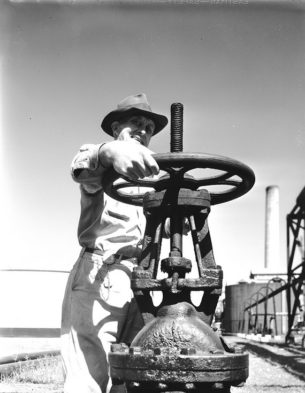 vintage workwear clothing-Worker operating oil pipeline valve, Texaco, TX, USA, 1944.