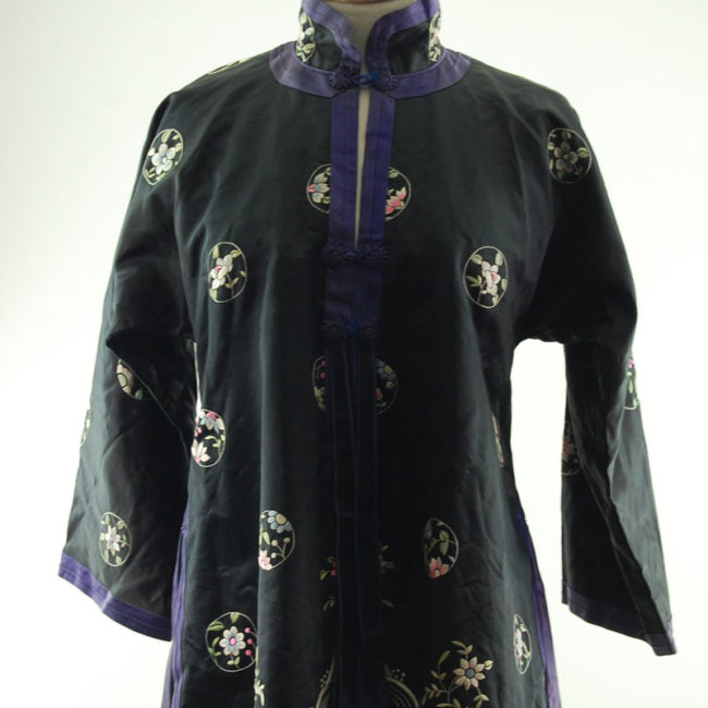 close up of Features a black block colour shirt with embroidered flowers and hills on the hemline with embroidered flowers.