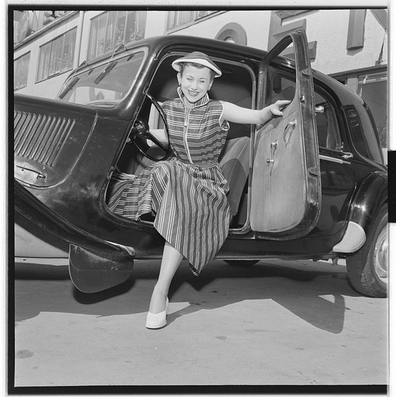 Woman weairing 1950s striped dress and white shoes alights from car, 1954 Woman weairing 1950s striped dress and white shoes alights from car, 1954